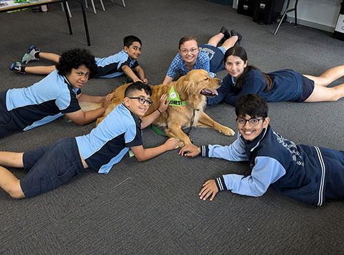 Kids in school uniforms lying on the ground with a therapy dog.